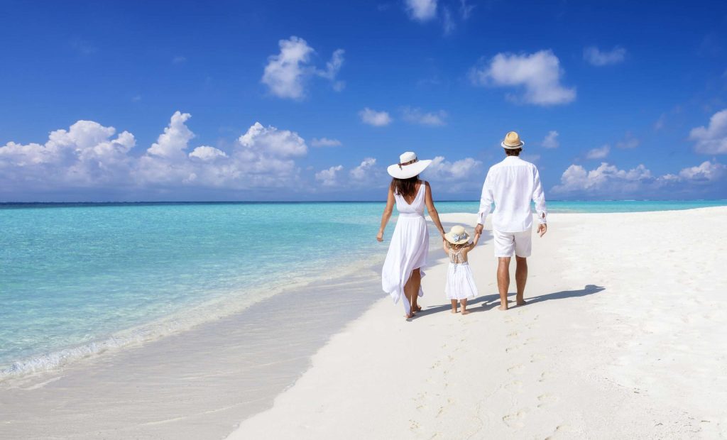 A beautiful family walks together on a tropical paradise beach in the Maldives with turquoise ocean and white sand during their vacation time
